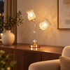 Rose gold twin-flower metal table lamp glowing on a walnut living room console